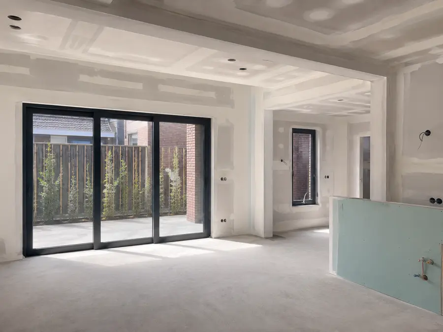 Binnenkant van een uitbouw tijdens de bouw: gestuukte wanden en plafond, schuifpui al geplaatst.