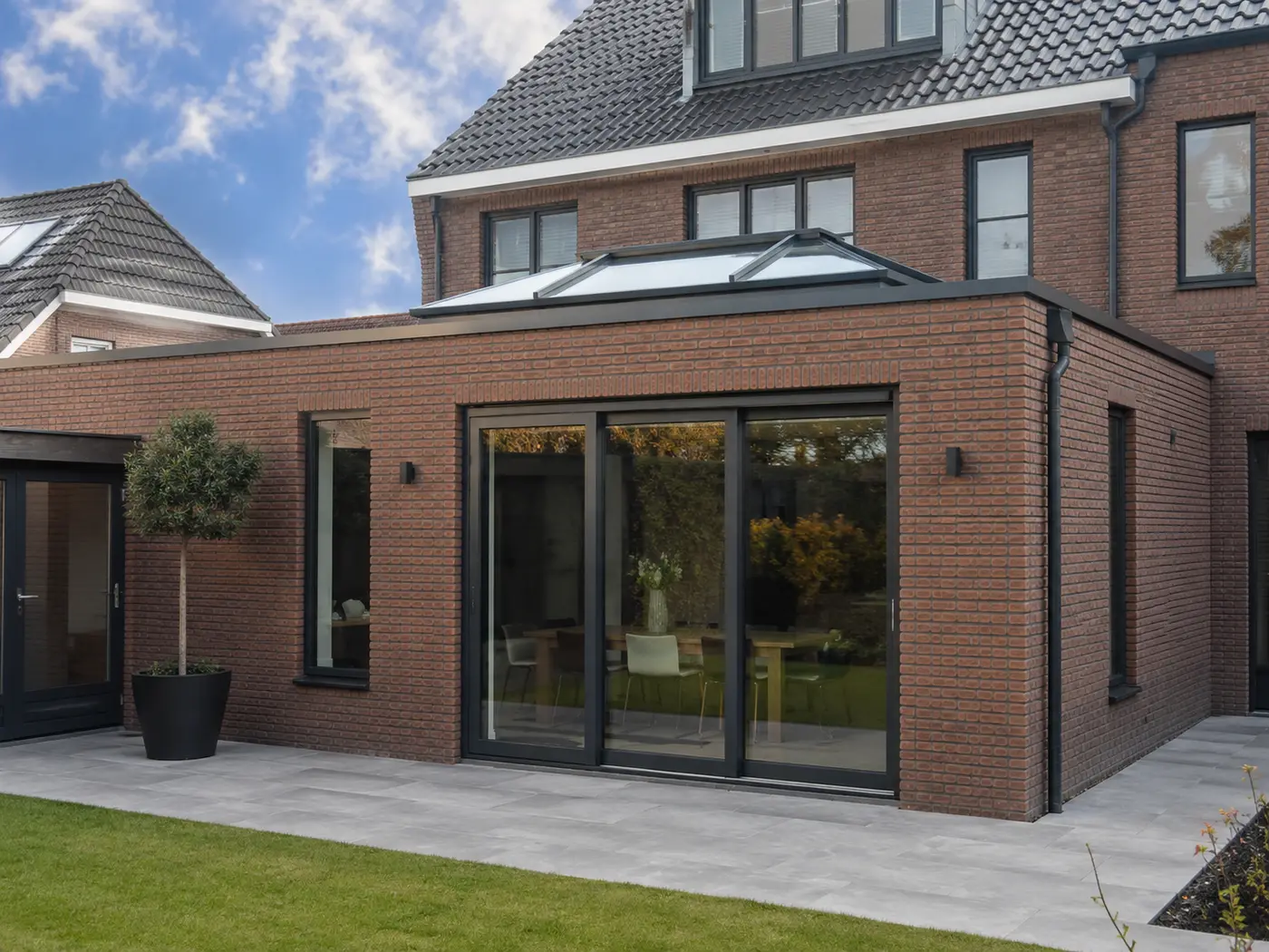 Uitbouw van rode baksteen met glazen lichtstraat en antracieten schuifpui, gezien vanuit de tuin.