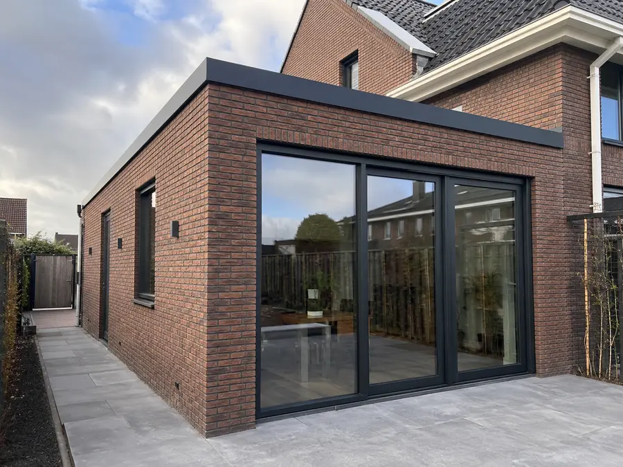 Uitbouw van rode baksteen met een driedelige schuifpui en een plat dak met antracieten daktrim.